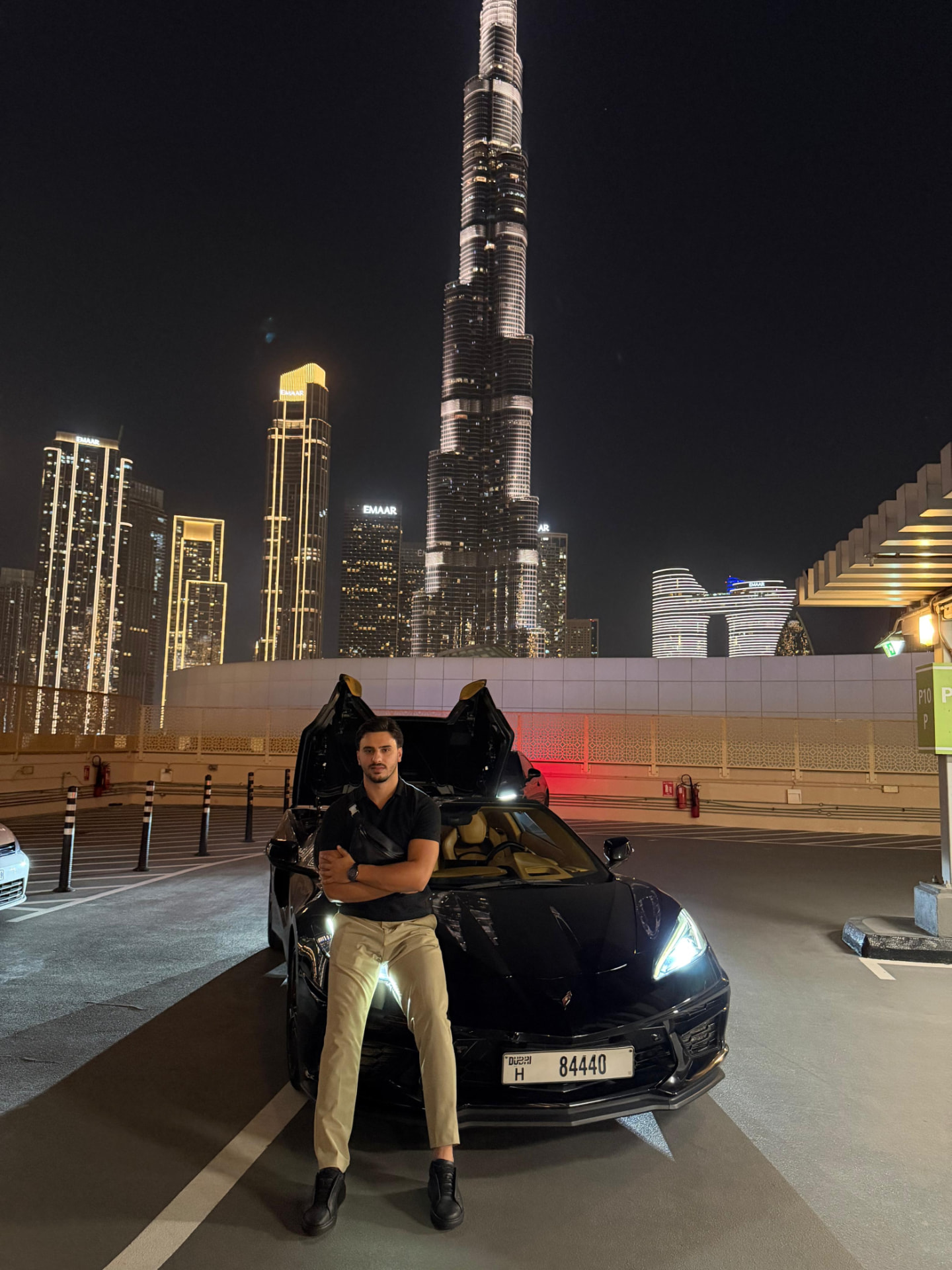 FX Kayss standing in front of a sports car with the Dubai skyline and Burj Khalifa behind him at night
